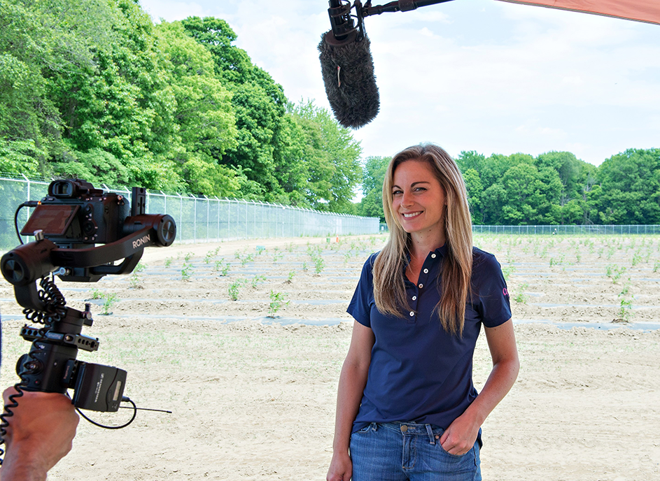 Deborah Sikkema is surrounded by camera equipment in front of a cannabis field