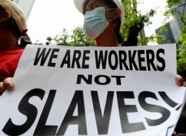 A photo of a person holing a sign reading &amp;quot;We are workers not slaves!&amp;quot;